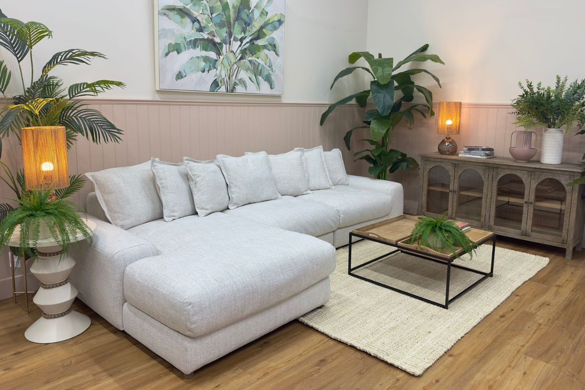 Eden neutral fabric modular corner sofa in a light, neutral living room with botanical wall art, indoor palm plants and rustic wooden furniture